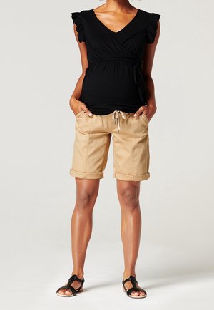 Top negro con mangas cortas con volantes, combinado con shorts beige enrollados que cuentan con un cordón. Sandalias planas negras completan el look.