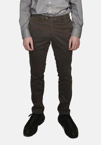 Pantaloni marrone scuro slim fit in misto cotone, con tasca frontale, cerniera lampo e sneakers nere con dettagli testurizzati.
