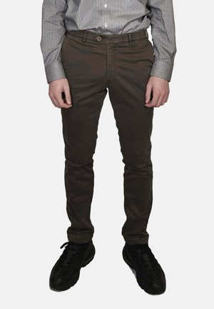 Pantaloni marrone scuro slim fit in misto cotone, con tasca frontale, cerniera lampo e sneakers nere con dettagli testurizzati.