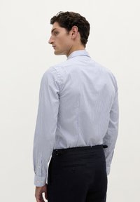 Cămașă cu dungi albastre și albe, cu mâneci lungi, guler și mansete cu nasturi, croi ajustat și țesătură netedă. Se asortează cu pantaloni închiși la culoare.
