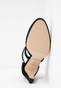 Chaussure à talon haut en suede noir avec un bout pointu. Côtés ouverts, fines lanières et semelle en caoutchouc texturée. Nom de la marque "Gabor" visible.