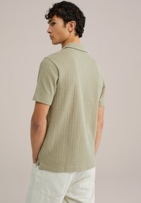 Short-sleeve, ribbed polo shirt in light green, featuring a collar, subtle texture, and side slits, paired with light beige trousers.