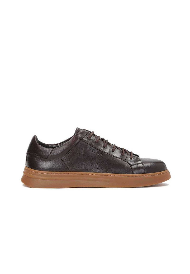 Barna bőr sneaker kerek orral, lapos gumitalppal és kontrasztos barna cipőfűzőkkel. Diszkrét márkajelzés található az oldalon. Simább felület.