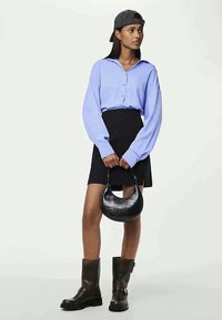 Svetlo modra srajca s gumbi, črna mini krila, črna torba s krokodiljim vzorcem, temno rjavi čevlji do kolen in siva kapica.