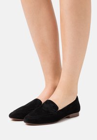 Mocassins en daim noir avec un talon plat, un bout arrondi et une texture lisse, dotés d'un design à enfiler et de détails de couture minimaux.