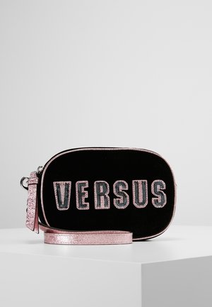 Sac bandoulière ovale noir avec bordure et sangle en paillettes roses, avec texte audacieux "VERSUS" en sequins roses et verts sur le devant.