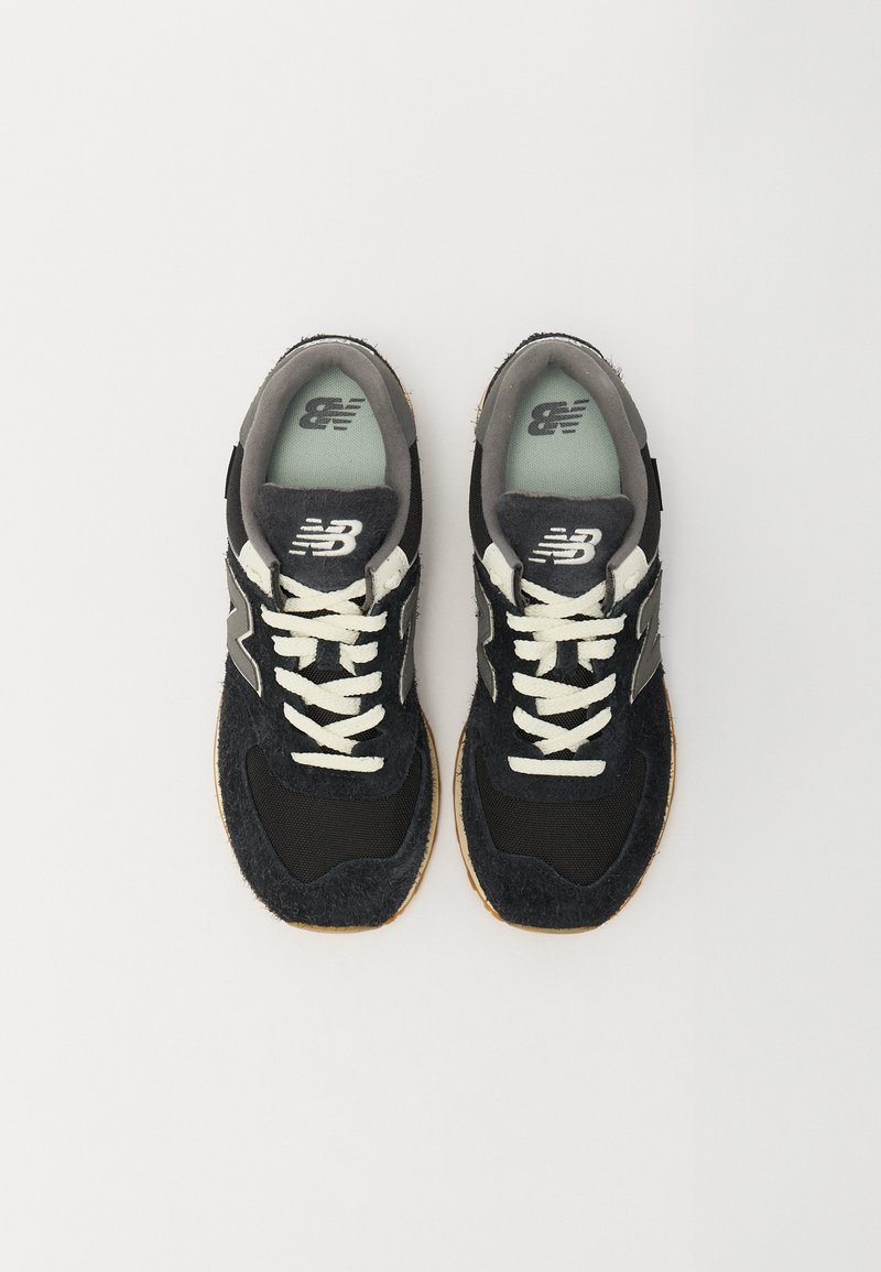 Baskets de sport noires et grises avec une tige texturée, des lacets blancs contrastants, une semelle en caoutchouc gomme et un logo sur le côté.