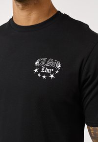 Μαύρο βαμβακερό t-shirt με στρογγυλή λαιμόκοψη, διακοσμημένο με λευκό γραφιστικό σχέδιο που αναγράφει «ELSE Ldn» και αστερίσκους στο αριστερό στήθος.