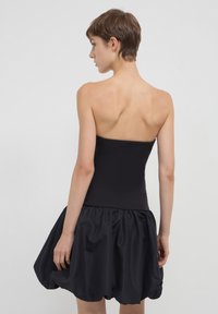 Abito nero senza spalline con un corpetto aderente e una gonna voluminoso e arricciata. Il tessuto ha una finitura liscia e una texture leggermente lucida.