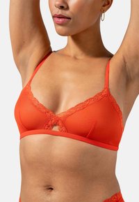 Orange bralette med spetsdetaljer i triangulär form, justerbara axelband och en nyckelhålsgrej i mitten. Slät textil.