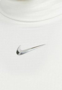 Vitt tyg med en silverfärgad Nike swoosh-logotyp nära kragen på en enfärgad bakgrund.