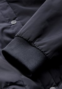 Schwarze, leichte Jacke mit einer glatten, glänzenden Oberfläche, Rippstrickbündchen und Druckknopfverschluss.