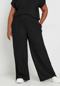 Mustat, teksturoidut leveälahkeiset housut, joissa on sivutaskut, yhdistettyinä lyhythihaiseen yläosaan, käytettävänä valkoisten tennareiden kanssa. Rentouttava ja mukava muotoilu.