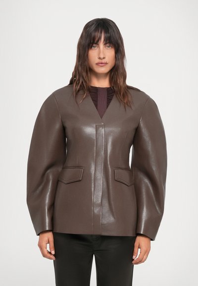 Blazer en cuir marron avec un col en V, des épaules structurées, deux poches avant et une finition brillante. Porté sur un haut texturé bordeaux.