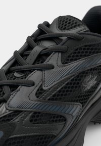 Black athletic shoe featuring a mesh upper with textured panels, lace-up closure, and a logo accent. Designed for comfort and breathability.