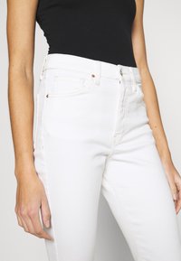 Jeans blancos de tiro alto hechos de denim, con un diseño clásico de cinco bolsillos, costuras sutiles y remaches en tono cobre en los bolsillos.