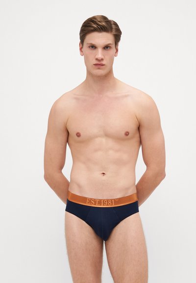 Boxeri pentru bărbați de culoare bleumarin, cu un elastic portocaliu pe care este marcat "EST.1981". Fabricat dintr-un material neted, având un design ajustat.