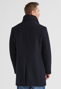 Marineblauer Wollmantel mit hohem Kragen, strukturierten Schultern und geradem Rückendesign. Verfügt über Seitennähte und minimalistische Details.