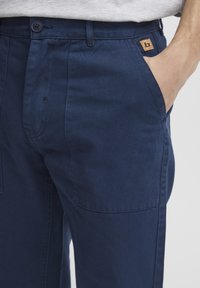 Pantalones azul marino de corte ajustado, confeccionados en algodón suave, con cierre de botón y un pequeño parche de cuero con la marca en la cintura.