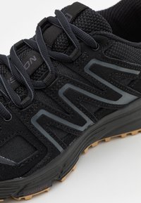 Svart och grå New Balance terränglöparskor med överdel i mesh, vadderad krage, snörning och strukturerad gummisula för bättre grepp.