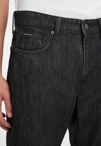 Černé džíny z denimu mají standardní pět kapsový design se stříbrným knoflíkem, jemným logem na zadní kapse a rovný střih nohavic.