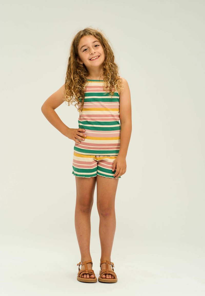 Top sin mangas a rayas en rosa pastel, amarillo y verde; pantalones cortos a juego con dobladillo con flecos. Sandalias marrones completan el conjunto.