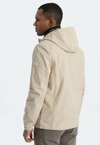 Beige wasserdichte Jacke mit Kapuze, ausgestattet mit einem Reißverschluss und Seitentaschen. Entworfen mit einer subtilen Textur und einem Logo-Patch am Ärmel.