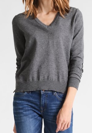 Un pull gris à col en V, fabriqué en tissu tricoté doux avec des manches longues et des poignets côtelés. Associé à un jean en denim bleu, affichant une coupe décontractée.