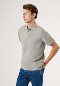 Polo gris clair en tissu doux et texturé, avec un col classique et des manches courtes, associé à un jean en denim bleu.