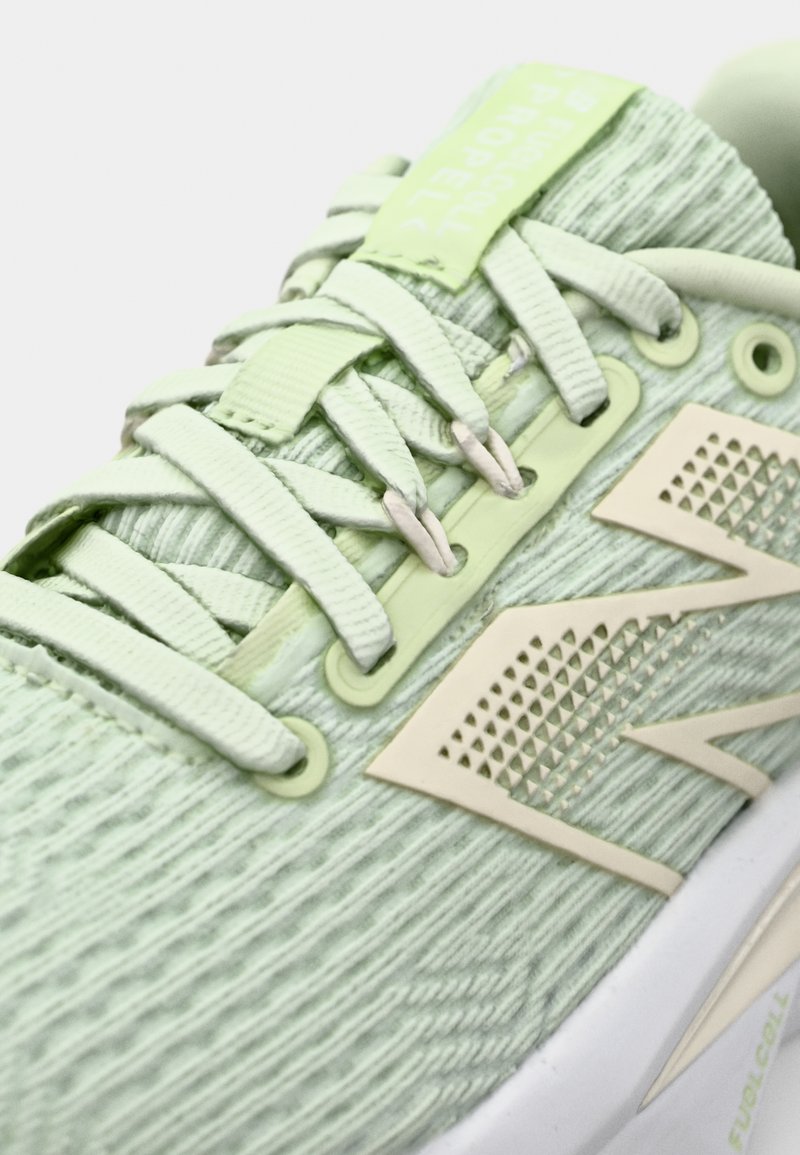 Chaussure de sport vert clair avec un dessus texturé, des lacets plats et un accent de marque couleur crème sur le côté avec un motif en diamant.