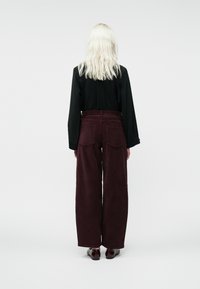 Platūs veliūriniai džinsai tamsiai burgundiškoje spalvoje, turintys aukštą liemenį ir dvi užpakalines kišenes. Suderinti su ilgu juodu marškinėliu.