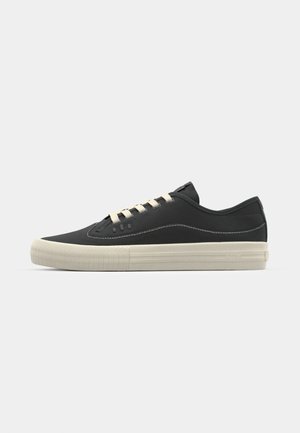 Black canvas sneakers with cream rubber soles, round toe, lace-up design, and contrast stitching. Minimalist design with no visible logos.