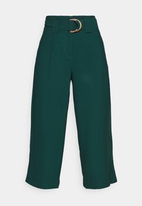 Gröna vida byxor i mjukt tyg, med en frontveck, bälteshällor och en rund metallspänne som accentuerar bältet.
