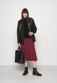 Zwarte leren button-up jacket, zwarte gebreide trui, bordeauxrode geplooide rok, zwarte laarzen en een zwarte tote bag. Eenvoudige texturen en kleuren.