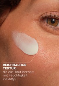 White cream with a rich texture applied to tanned skin. Smooth surface and visible sheen indicate hydration. Close-up of skin detail.