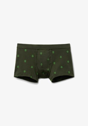 Tmavě zelené boxerky s malými jasně zelenými vzory želv rovnoměrně rozmístěnými po látce, položeny na bílém pozadí.