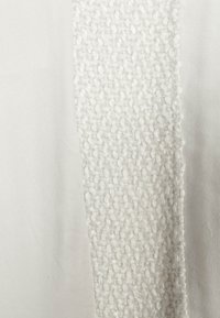 Gros plan d’un tissu blanc montrant un tissu lisse sur les côtés et une bande tissée en fil bouclé texturé au centre.