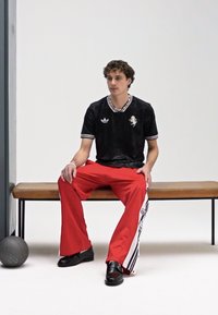 Maillot de sport noir avec accents blancs et emblème, associé à un pantalon de survêtement rouge ample avec des bandes latérales, et des chaussures noires. Ballon de basket gris à proximité.