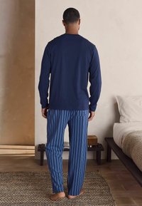 Jūras zila garām piedurknēm krekls, apvienots ar zili svītrainiem pidžamu biksēm. Audums izskatās mīksts; biksēm ir elastīgs jostasvieds un aizmugurējā kabata.