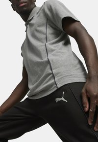 Grå polo shirt med korte ærmer, der har en slank pasform og kontrastsyninger, parret med sorte sweatpants, der viser et logo.