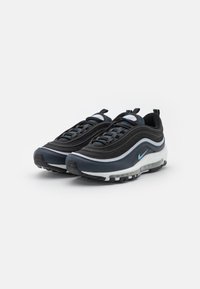 Zapatillas negras y azul marino con parte superior de malla, diseño ondulado, media suela blanca y un logo azul claro. Cuentan con una suela acolchada y agarre texturizado.