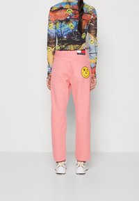 Pantalones de mezclilla rosas con un ajuste relajado, que presentan un gran parche de cara sonriente y texto "NY" en el bolsillo trasero. Top de manga larga con un patrón multicolor.