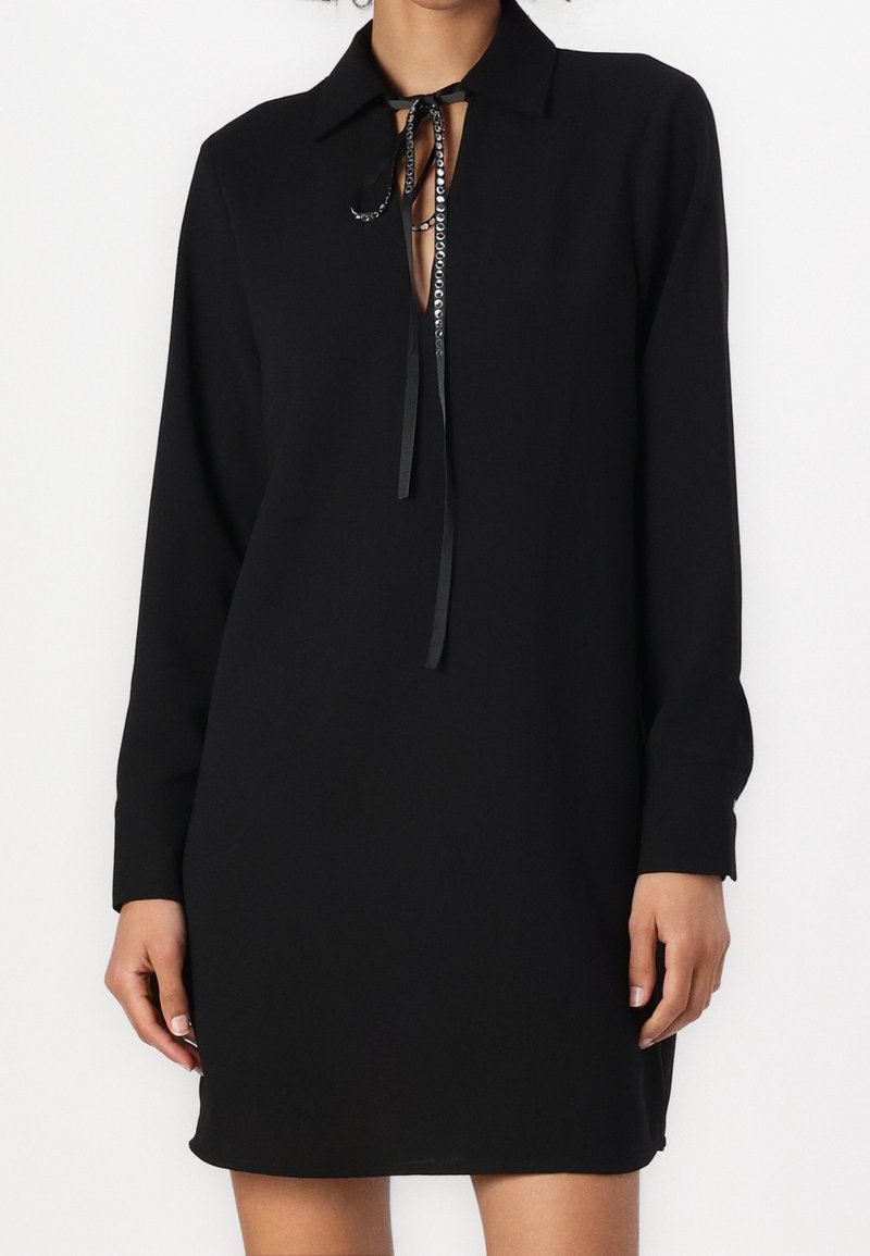 Robe noire avec un col, des manches longues et un décolleté en forme de clé. Présente un lacet fin et une texture de tissu lisse.