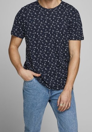 T-shirt en coton bleu marine avec un motif blanc répété de petits dessins, manches courtes et col rond, associé à un jean bleu clair.