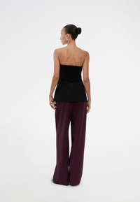 Black strapless top with gathered back, paired with loose, dark burgundy wide-leg pants. Smooth fabric texture with simple design.
