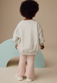 Grauer Sweatshirt mit lockerer Passform, kombiniert mit flared gestreiften Hosen in Rosa und Weiß. Weiße Sneakers mit fransigen Akzenten.