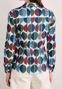 Printed long-sleeve shirt with a white background, featuring multicolored circular patterns in red, green, and blue, with textured accents.