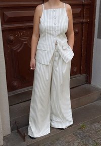 White pinstriped outfit featuring a sleeveless top with buttons and pockets, paired with wide-leg trousers, both in a lightweight fabric.