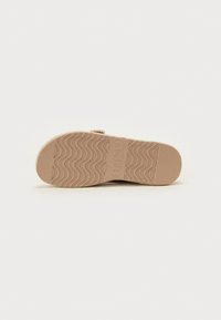 Semelle de chaussure avec une texture ondulée, fabriquée en caoutchouc brun clair ; présente un logo et un design de bout rond ; surface plate et antidérapante.