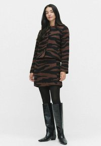 Brown and black striped knit jacket and skirt set paired with knee-high black croc-embossed boots. Model stands against a plain background.